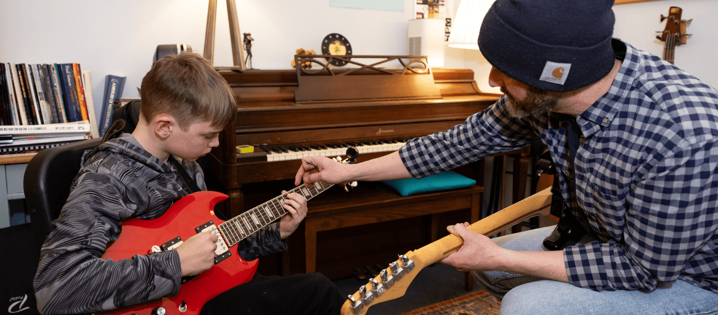Guitar Lesson with instructor pointing to neck of boy's red guitar