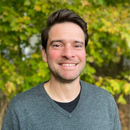 Brian O'Shaughnessy, voice teacher, smiles in front of a background of trees.