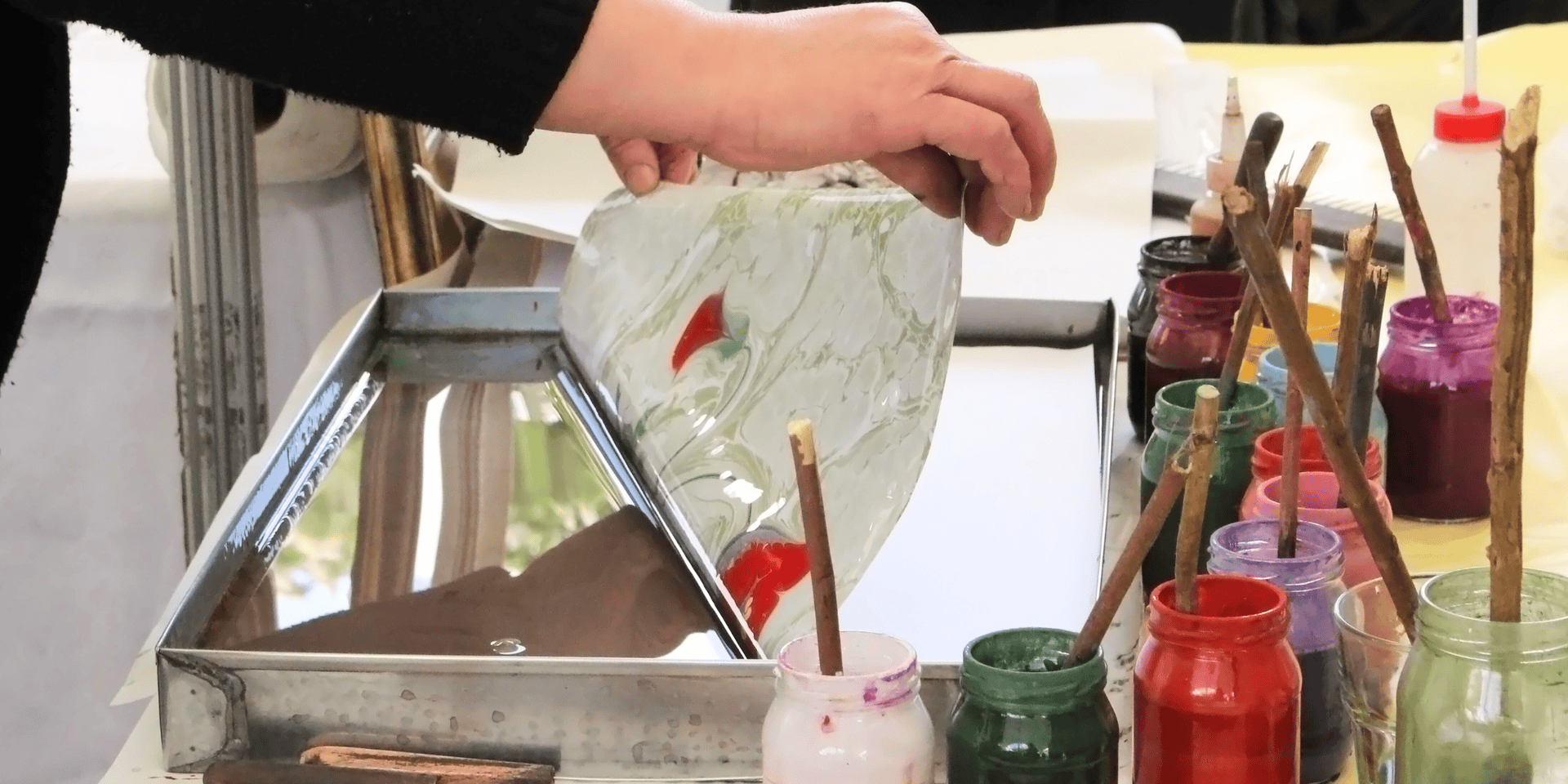 Hands lift paper into paper marbling water