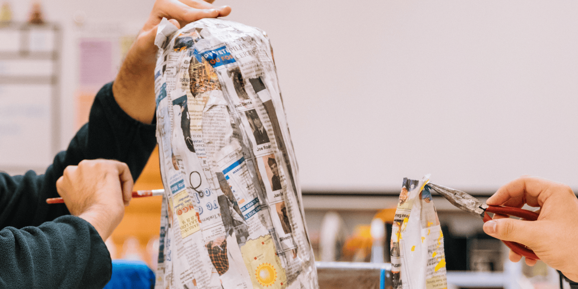 Hands work on a Papier-Mâché sculpture, while another person holds a piece of Papier-Mâché up to add