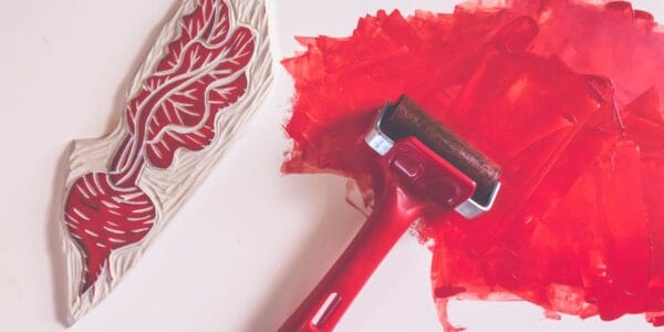 A block print of a radish next to a paint roller and red paint