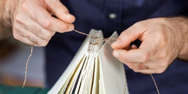 Hands work on bookbinding paper with twine