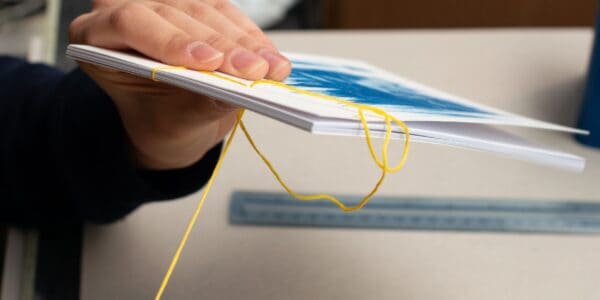 Hands work on bookbinding white paper with yellow thread